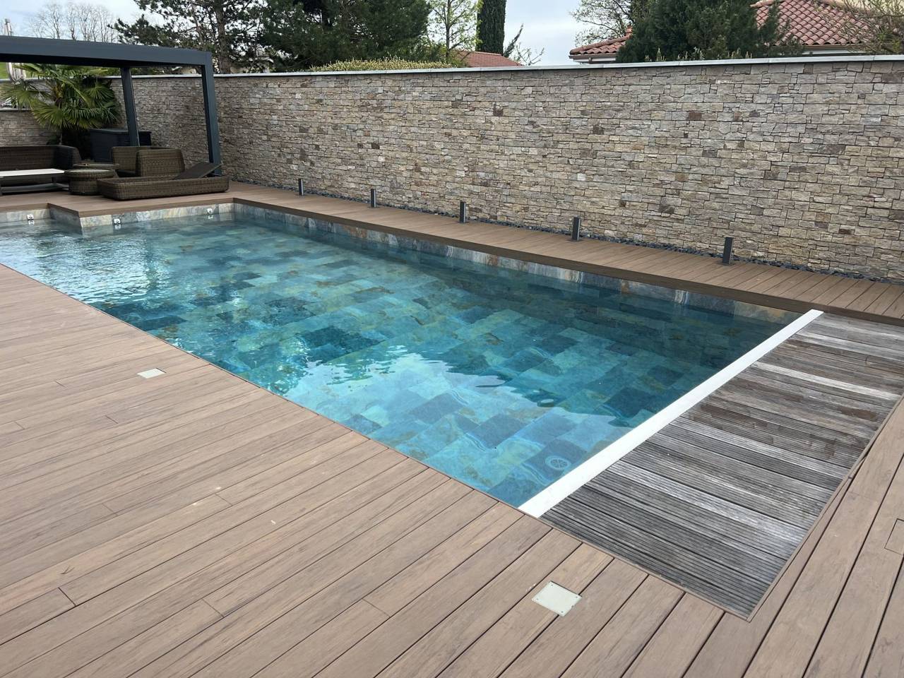 Piscine maçonnée terminée avec plage bois et mur en pierre, réalisée par Lyonblue